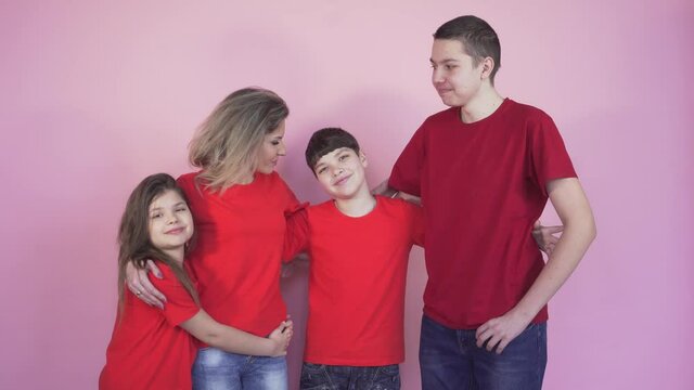 A young beautiful mother is hugged and kissed on the cheek by children, a boy and a girl. Pink background.