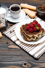 portion of Classic tiramisu dessert with raspberries, cup of espresso and coffee maker on wooden background