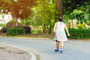 Fototapeta na wymiar Back view of a Asian elderly woman wears earphone to listening song walking and jogging for good health in public park.Senior jogger in nature. Older female enjoying Peaceful nature.Healthcare concept