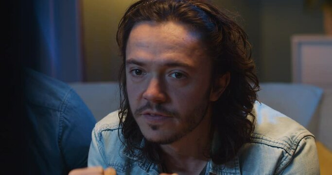 Close up of worried Caucasian male football fan sitting with friends at TV screen in dark living room and watching match. Scoring goal or winning game concept. Cheerful man celebrating football win.