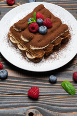 portion of Classic tiramisu dessert with raspberries and blueberries on wooden background