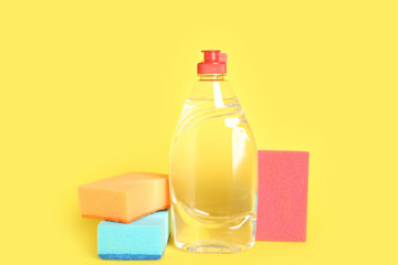 Bottle of detergent and sponges on yellow background