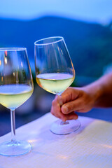 Hand with glass of cold dry white wine served outdoor in cafe at night in Italy