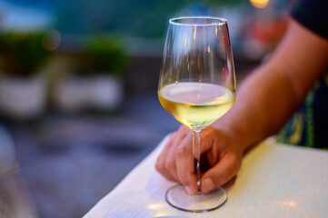 Hand with glass of cold dry white wine served outdoor in cafe at night in Italy