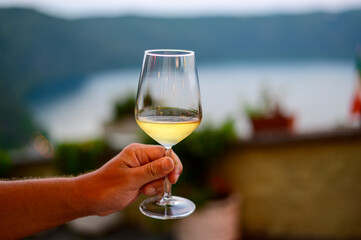 Hand with glass of cold dry white wine served outdoor in cafe at night in Italy