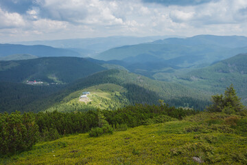 Naklejka na ściany i meble Mountain landscape. A view of the mountains with green meadows and coniferous forests against the background of beautiful clouds. Carpathians