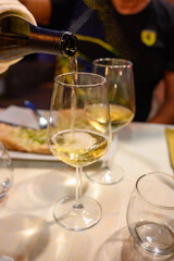 Pouring in glass  cold dry white wine in outdoor cafe at night in Italy