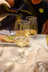 Pouring in glass  cold dry white wine in outdoor cafe at night in Italy