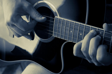 Detail of a man playing an acoustic guitar, duotone color