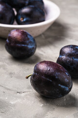 Fresh ripe plum fruits with water drops in wooden bowl on stone concrete background, angle view macro