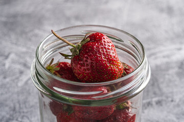 Fresh ripe strawberry fruits in glass jar, summer vitamin berries on grey stone background, angle view macro