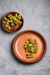 Fresh ripe white grape berries in wooden plate and bowl on stone concrete background, top view