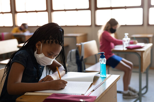Black African American Girl wearing face mask writing while sitting on her desk at school