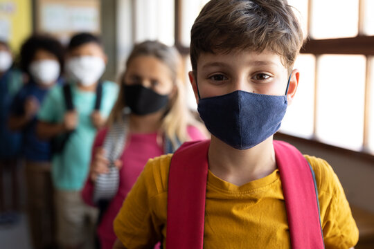 Group Of Kids Wearing Face Masks With Bag Packs Standing In A Queue At School