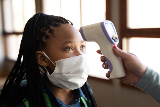 Girl wearing face mask getting her temperature measured in class at school