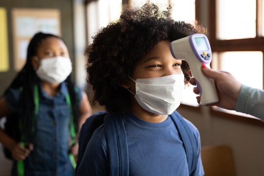 Black African American Boy wearing face mask getting his temperature measured in class at school