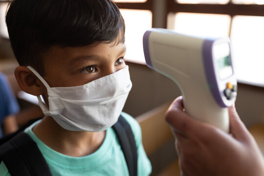 Boy wearing face mask getting his temperature measured in class at school
