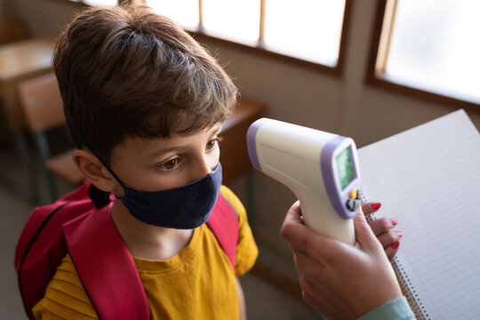 Boy wearing face mask getting his temperature measured in class at school