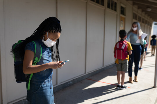 Black African American Girl wearing face mask using smartphone at school
