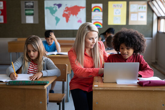 Female teacher and boy using laptop in class at school
