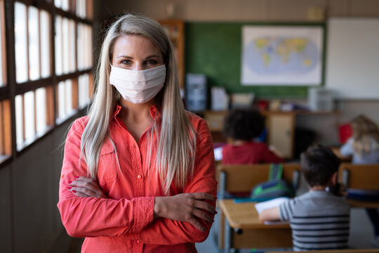 Portrait of female teacher wearing face mask standing with her arms crossed in class
