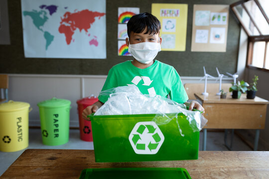 Portrait of boy wearing face mask holding a recycle container in class at school