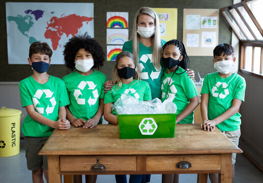 Portrait of female teacher and group of kids wearing face masks with recycle container at school