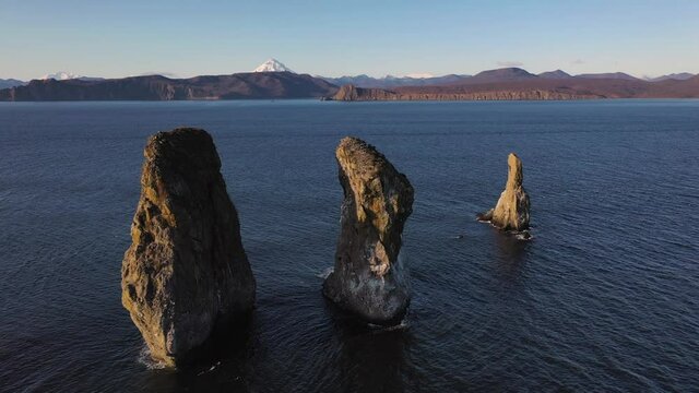 Autumn scenery, beautiful sunrise over Avacha Bay on Russia's Kamchatka Peninsula, and the famous Three Brothers Rock. The waters of the Pacific Ocean. In the background is the Avachinsky volcano.