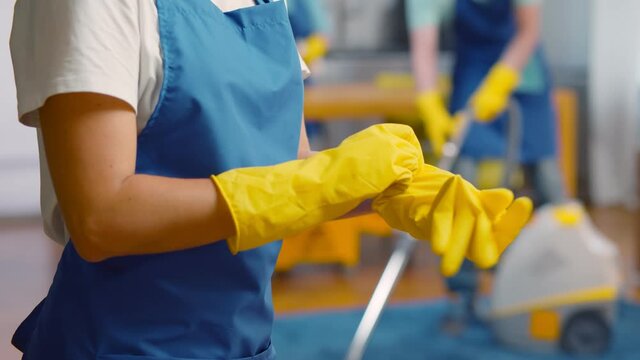 Close up of maid in apron putting on rubber gloves for cleaning apartment
