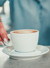 Closeup female barista hands holding cup of aromatic latte or cappuccino coffee in bar or cafe