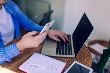 Cropped image of skilled male user connecting to bluetooth for sharing files between smartphone and laptop devices during e learning, man searching education information for planning web project