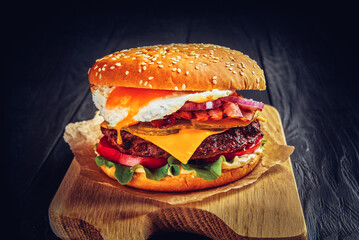 Beef burger with melted cheese and bacon and egg on wooden background