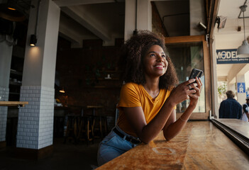 Beautiful ethnic women gazing upward and sitting at window sill of eco coffee shop. 