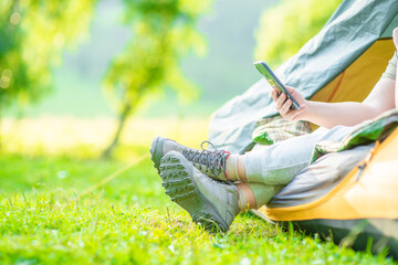 Hiker sits inside tend and checks a smartphone for internet contacts or work while sits inside...