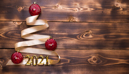 A Christmas tree made of gold ribbon with the numbers 2021 is decorated with red balloons on a dark wooden background. Flat lay. Space for text. New year, Santa hat.