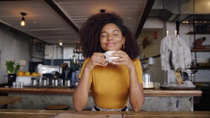 Beautiful smiling female customer sipping hot coffee while sitting in trendy cafe.