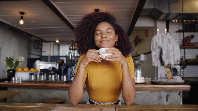 Beautiful smiling female customer sipping hot coffee while sitting in trendy cafe.