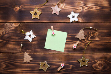 Christmas flat lay of wooden stars, fir trees and clothespins on a dark background with a square sheet for notes in the center. New year's frame, space for text. Xmas toys, to do list, a postcard