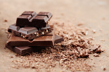 Composition of bars and pieces of different milk and dark chocolate, grated cocoa on a brown background side view close up