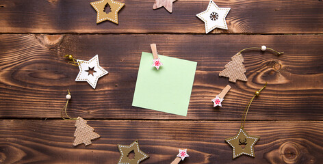 Christmas flat lay of wooden stars, fir trees and clothespins on a dark background with a square sheet for notes in the center. New year's frame, space for text. Xmas toys, to do list, a postcard