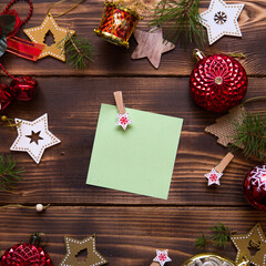Christmas flat lay of red balloons and wooden stars and clothespins on a dark background with a square sheet for notes in the center. New year's frame, space for text. Xmas toys, beads, pine branches