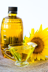 sunflower oil poured into glass saucepan is on a canvas napkin. near a bottle of oil and flowers. on white background