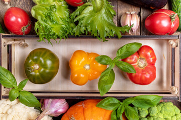 Top view fresh ripe farm vegetables in small wooden box and on table close up. Horizontal orientation. Advertising healthy natural food. Vegetable harvest.