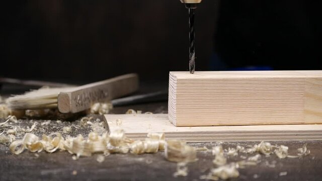 Anonymous craftsman drilling timber board with electric tool in slow motion on messy table in workshop