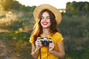 Smiling woman with closed eyes and with a camera in her hands in a hat on nature