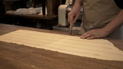 Male hands cutting dough rolled on big wooden table at the restaurant kitchen. Making ravioli, cutting big long slice of raw dough, italian cuisine