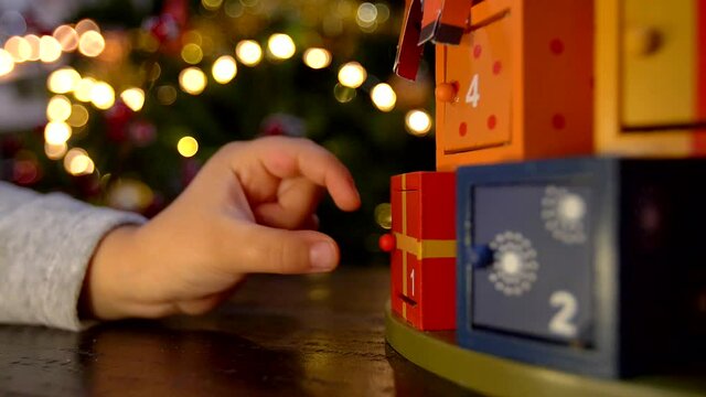 child hand opening advent calendar wooden door and finding a surprise little word paper gift. Close up shot
