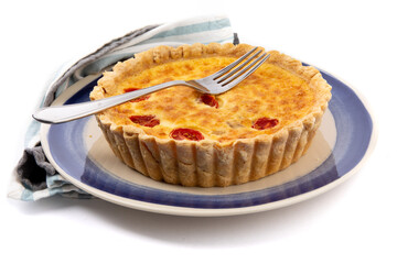 a whole cheese quiche with tomatoes on a blue plate with a serving fork isolated on white