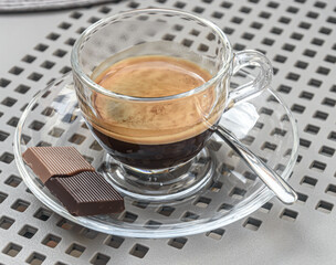 A cup of espresso coffee with chocolate cube on the side