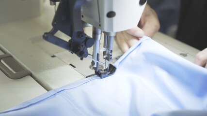 Sewing on machine, hands and blue cloth close up. Lens flare of sewing process, female hands on white machine with blurry effect side shot
